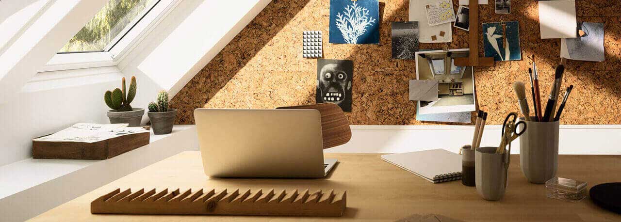 Un bureau avec ordinateur portable, lampe et photographies au mur est placé à côté de deux fenêtres de toit VELUX.