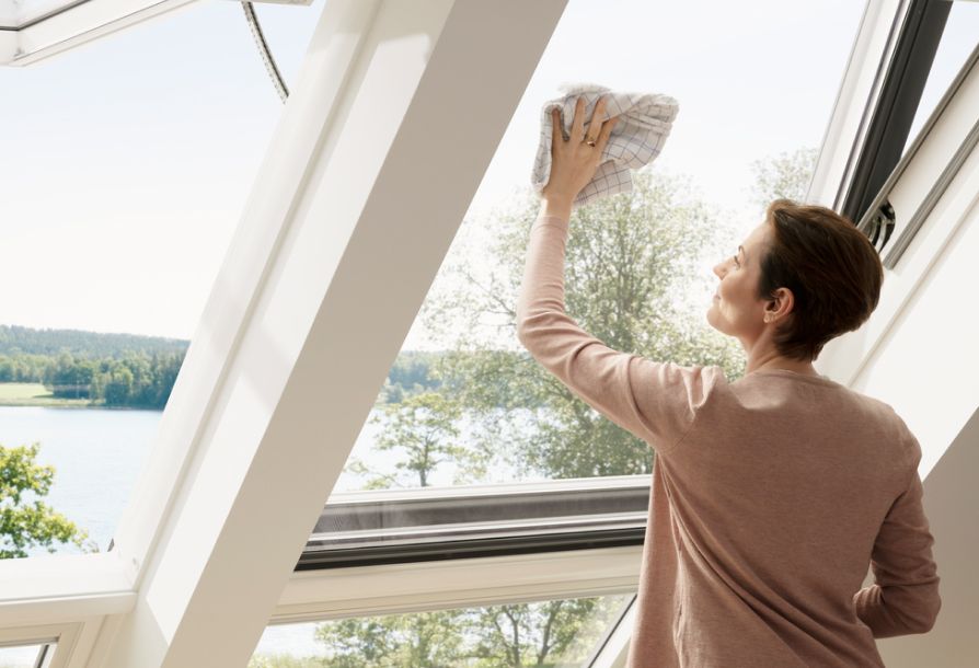 Donna che pulisce la sua finestra per tetti VELUX dall'interno nel suo soggiorno.