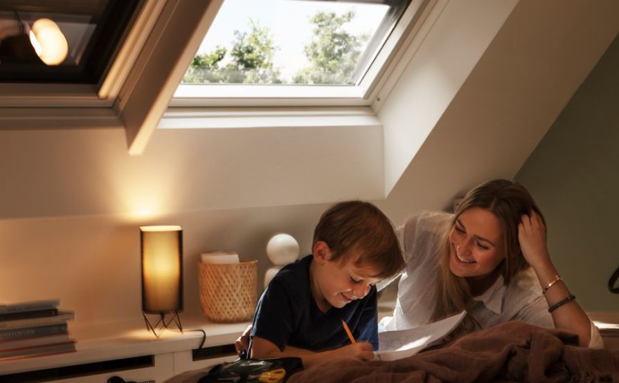 Junge liest seiner Mutter in seinem Schlafzimmer aus einem Buch vor, mit zwei VELUX Dachfenstern mit Verdunkelungsrollos im Hintergrund.