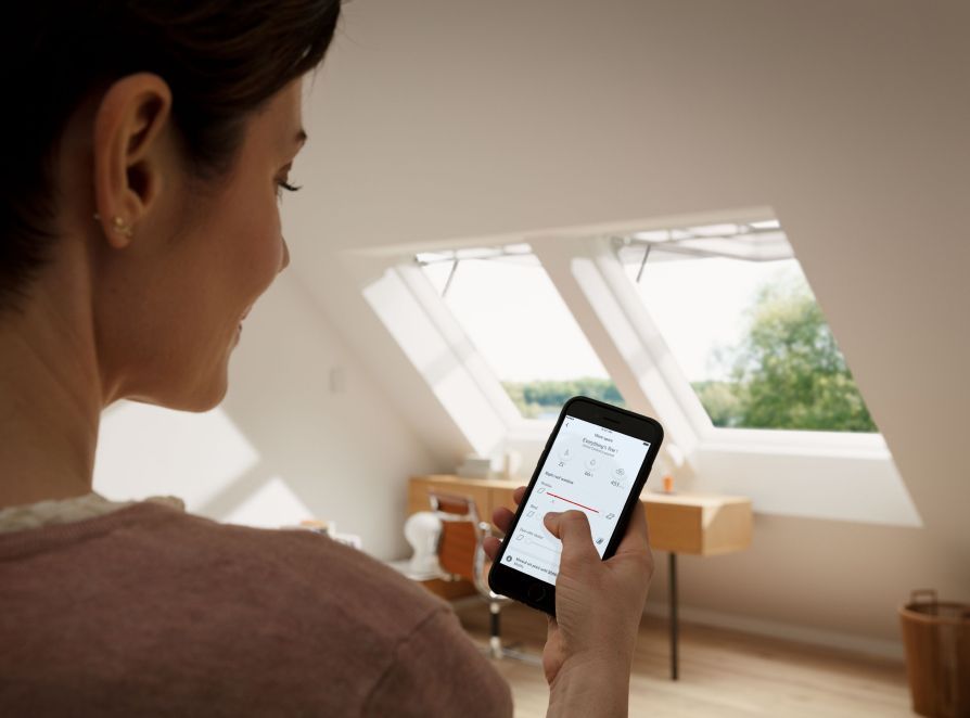 Femme activant ses deux fenêtres de toit VELUX à l'aide de l'application VELUX ACTIVE de son smartphone.