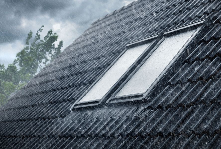 La pluie tombe à l'extérieur sur deux fenêtres de toit VELUX installées sur un toit de tuiles noires.