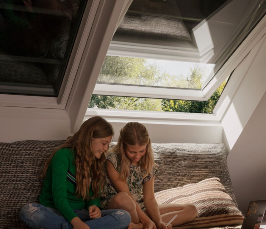 Zwei Mädchen in einem Kinderzimmer sitzend, mit zwei VELUX Dachfenstern im Hintergrund, mit VELUX Verdunkelungsrollos.
