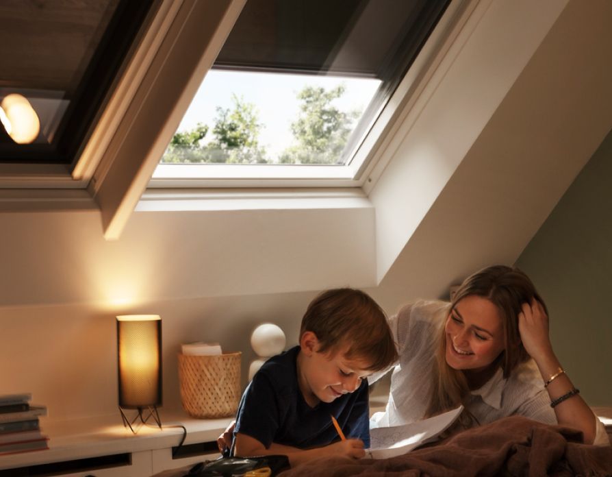 Junge liest seiner Mutter in seinem Schlafzimmer aus einem Buch vor, mit zwei VELUX Dachfenstern im Hintergrund, mit Verdunkelungsrollos.
