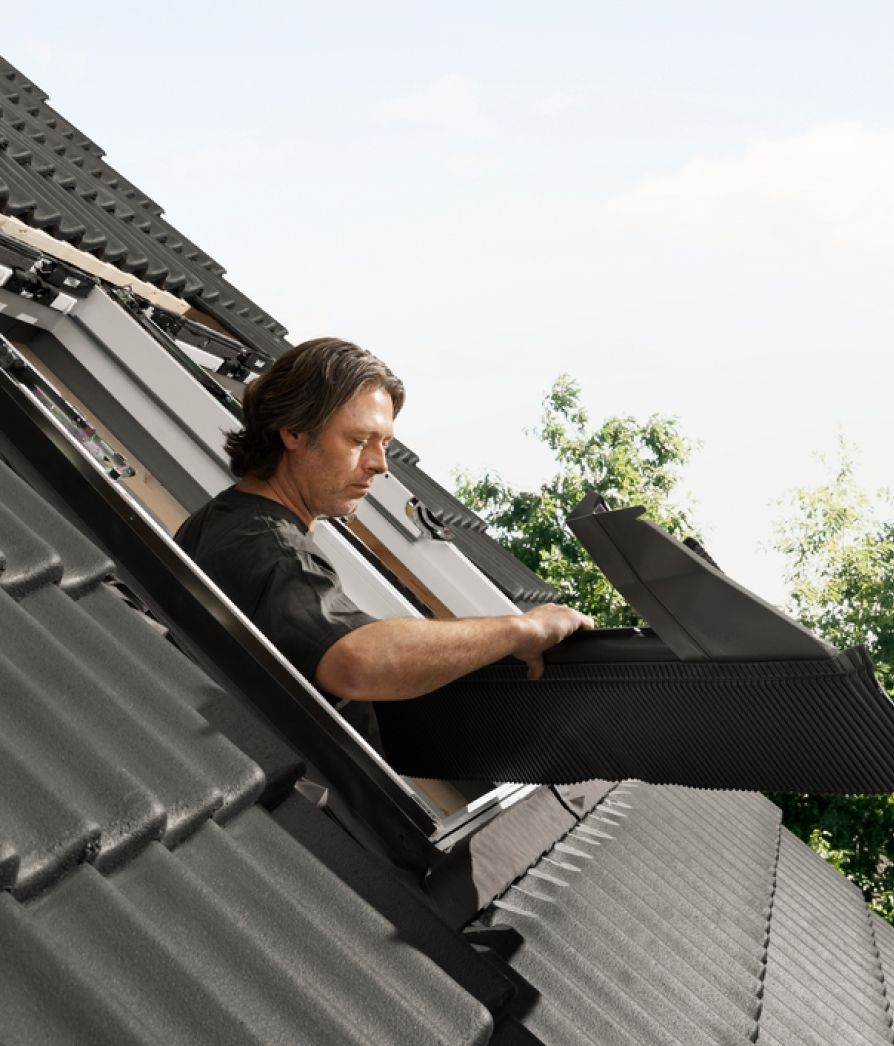 Handwerker beim Einbau eines neuen VELUX Dachfensters auf einem Dach mit schwarzen Ziegeln.