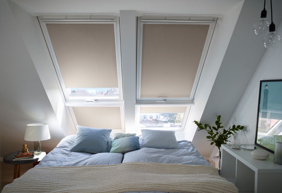 Ein Schlafzimmer mit vier VELUX Dachfenstern, die mit cremefarbenen Verdunkelungsrollos abgedeckt sind