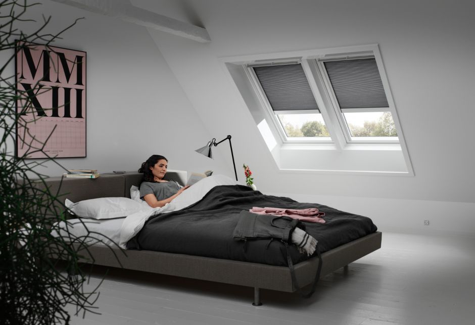 Eine lesende Frau in ihrem Bett mit zwei VELUX Dachfenstern auf der schrägen Fensterfläche neben sich.