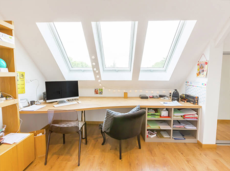 Un ufficio in casa luminoso con tre lunghe finestre per tetti VELUX posizionate sopra la scrivania.