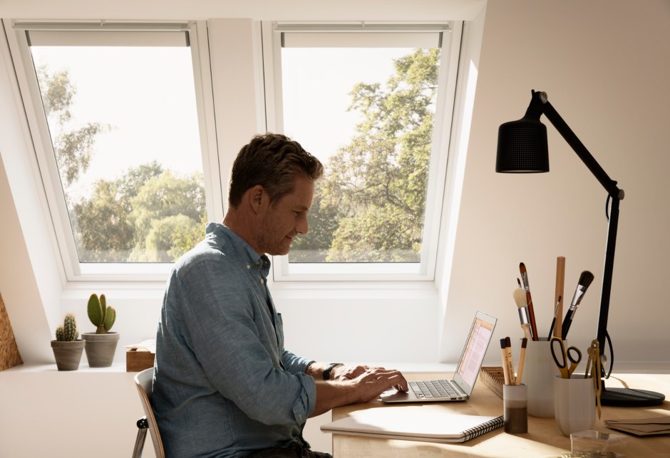 un uomo è seduto alla sua scrivania, sullo sfondo ci sono due finestre per tetti VELUX.