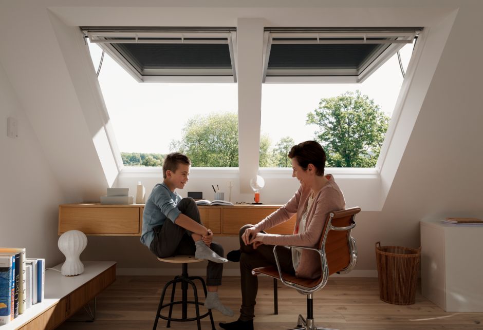 Eine Frau und ein Junge unterhalten sich, vor zwei VELUX Klappflügelfenstern sitzend.