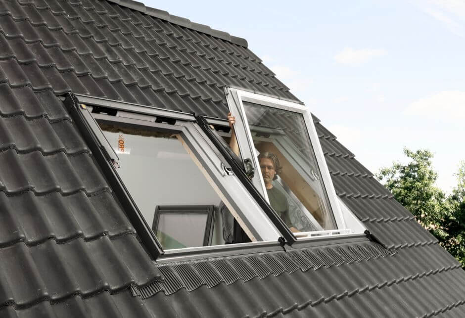 Un installateur place l'une des deux fenêtres de toit VELUX sur un toit noir.